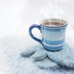 pexels-photo-3334510-3334510 A steaming blue coffee mug sits on knitted gloves amid snowfall, evoking coziness.